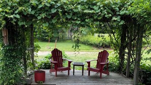 A wooden deck with a stone pathway leading to a seating area with two Adirondack chairs and a small table.