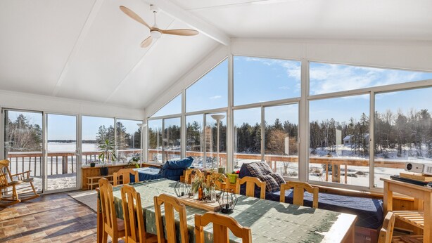 A sunlit dining area with a large table, chairs, and a view of a snowy landscape through large windows.