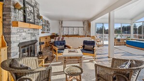 A spacious living area with a stone fireplace, comfortable seating, and large windows offering a view of the outdoors.