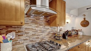 Una cocina con estufa a gas, gabinetes de madera, salpicadero de ladrillo y encimera con utensilios de cocina y un botellero.