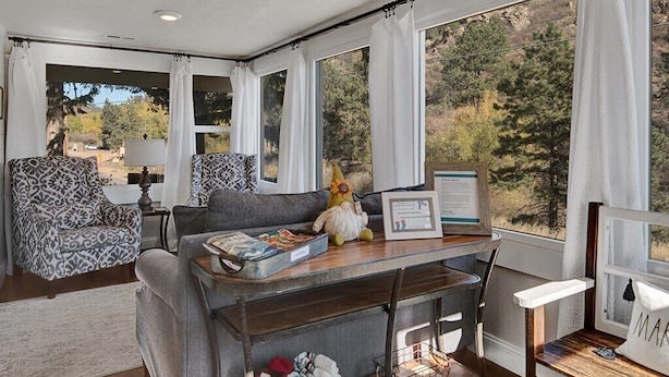 Una sala de estar acogedora con un sofá, una mesita de centro y vistas a un bosque a través de amplias ventanas.