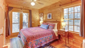 A cozy wooden cabin bedroom with a large bed, a ceiling fan, and a window with curtains. - 'Toccoa Waterfront Hideaway:' Hot Tub & Fire Pit! (Mineral Bluff)