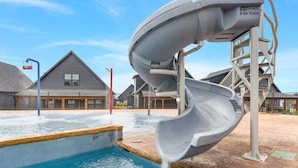 Una estructura de tobogán de agua sobre una piscina, con un edificio al fondo.