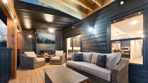 Un espacio exterior acogedor con mobiliario de mimbre, una chimenea y un ventanal que ofrece vistas del interior.