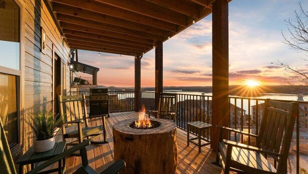 Una terraza de madera con un pozo de fuego, asientos exteriores y vistas al atardecer sobre el agua.