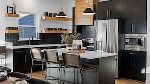 Una cocina moderna con armarios negros, electrodomésticos de acero inoxidable y una isla central con taburetes de bar.
