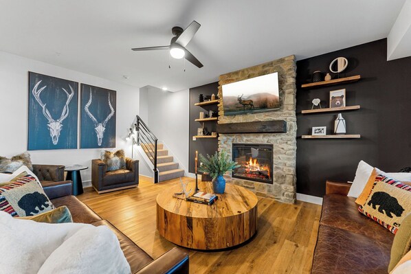 A modern living room with a stone fireplace, leather sofas, a round coffee table, and artwork on the walls.
