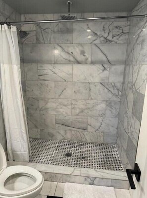Eine Dusche mit Marmorwänden und gefliestem Boden.