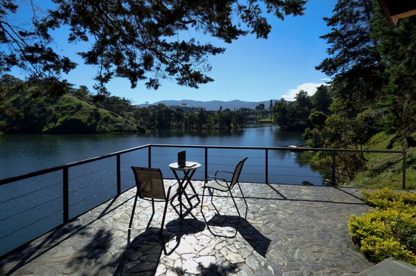 A stone deck with two chairs and a table overlooking a lake, surrounded by trees and hills. - Cottage on the Lake:Private Cabin with Jacuzzi in Guatapé, near Piedra del Peñol (Peñol)