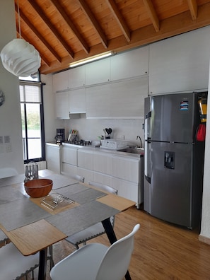 A modern kitchen with white cabinets, a stainless steel refrigerator, and a dining area with a wooden table and chairs. - Cottage on the Lake:Private Cabin with Jacuzzi in Guatapé, near Piedra del Peñol (Peñol)