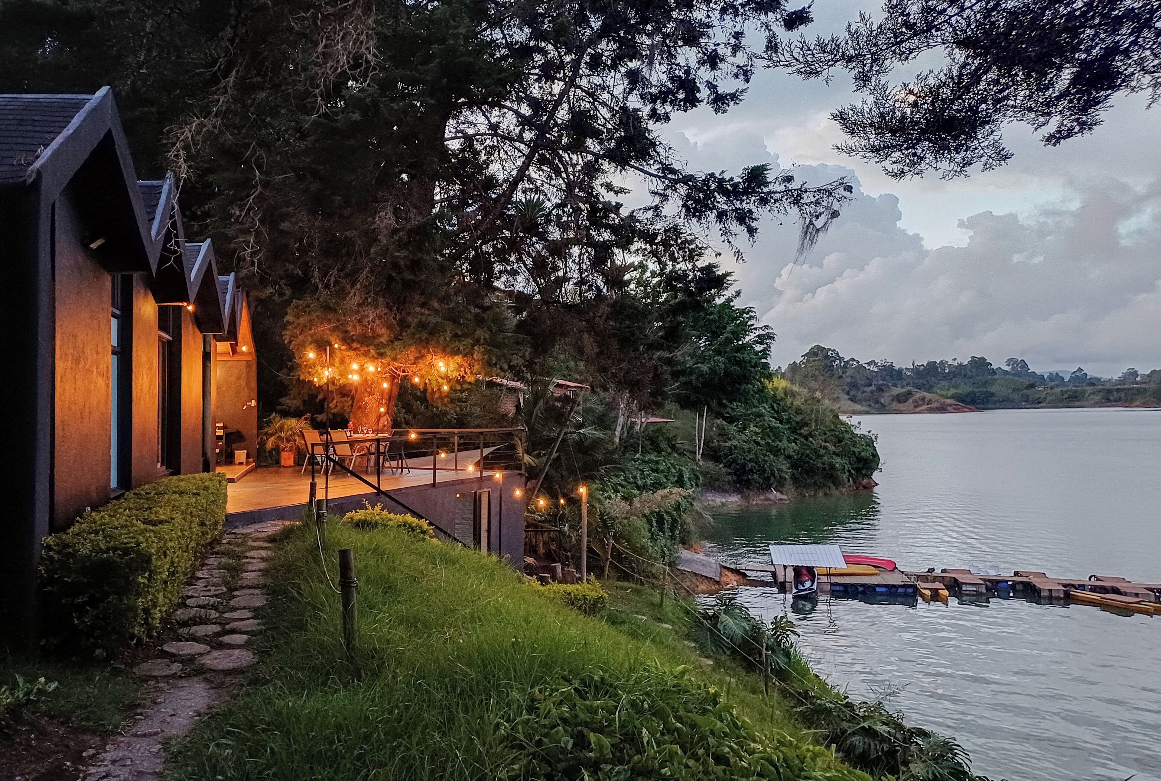 A lakeside property with a pathway leading to a deck, surrounded by lush greenery and a dock with canoes.