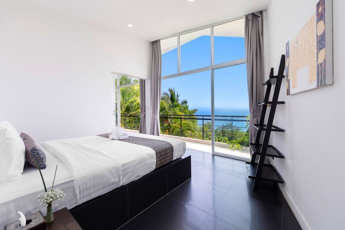 Une chambre moderne avec un grand lit, une vue sur l’océan et un balcon agrémenté d’une échelle noire.
