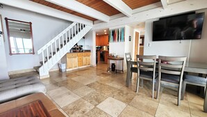 A spacious living area with a staircase, a dining table with chairs, and a kitchen in the background. - 3BR/2BA OCEANFRONT - Nohonani 403 -  Stunning Views From Every Room, AC & Pool (Lahaina)