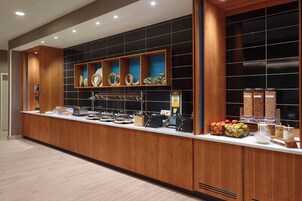 A buffet counter with various food items, a coffee machine, and a fruit display.