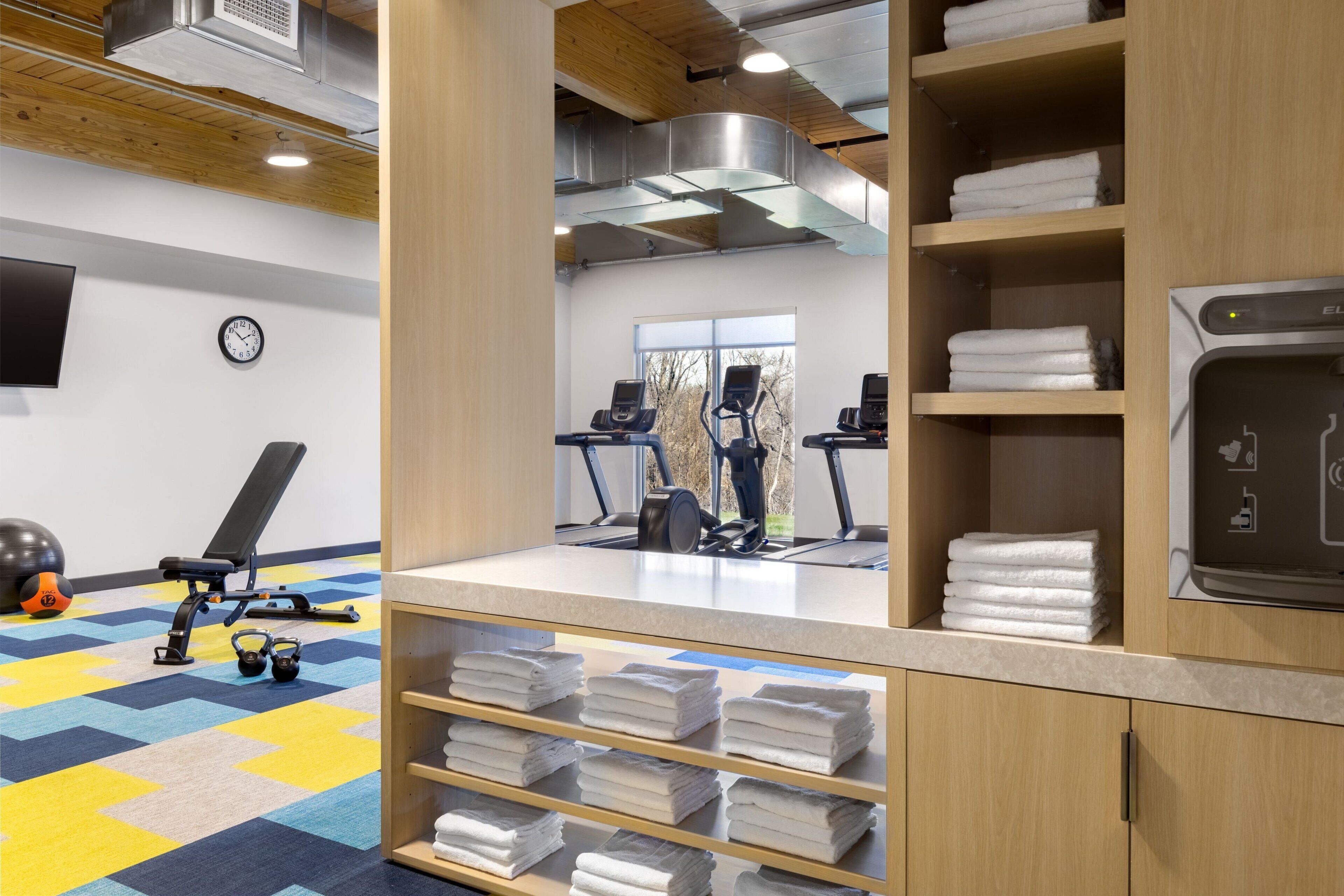 Et fitnessrum med træningsudstyr, et ur og pænt foldede håndklæder.