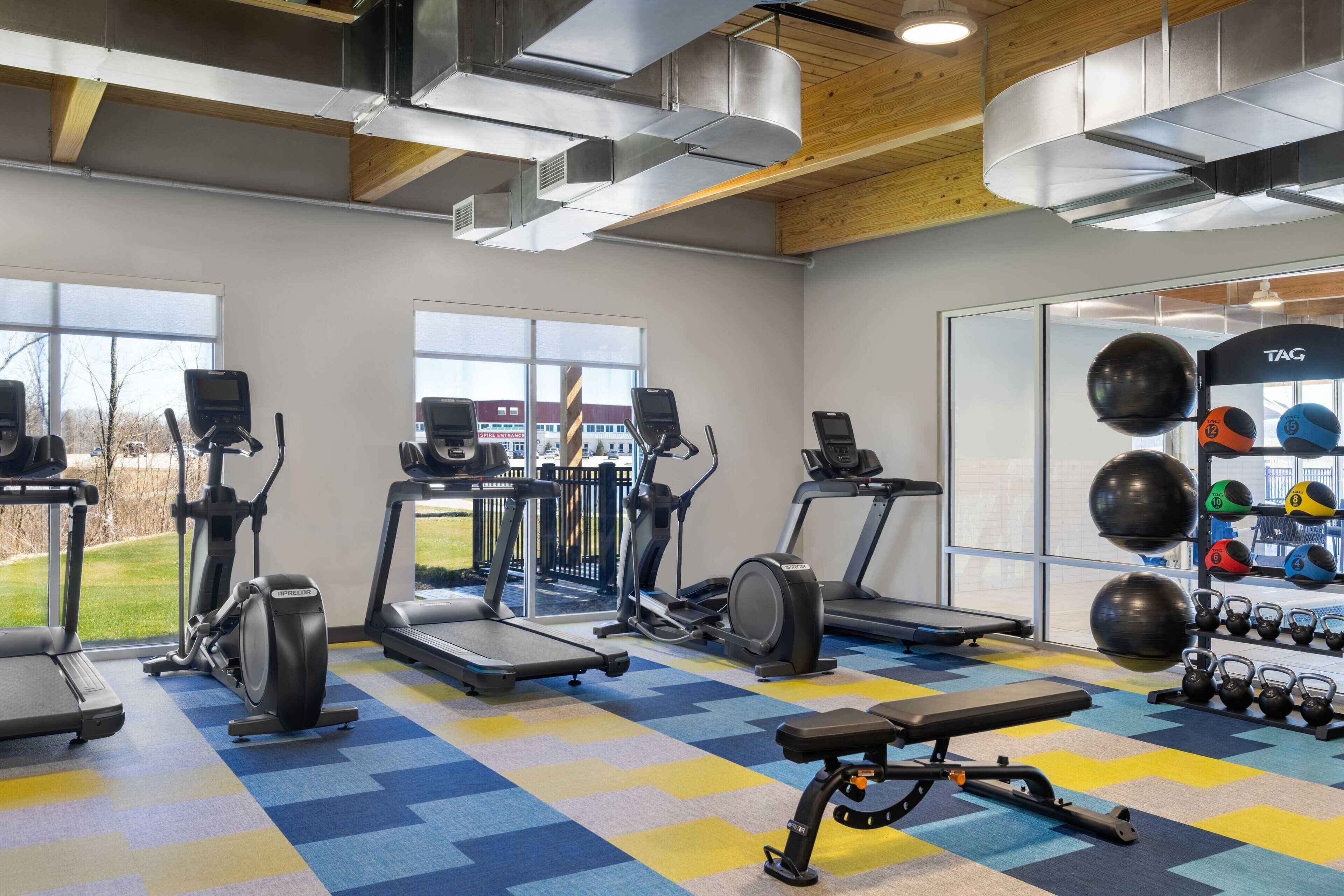 A gym with treadmills, elliptical machines, a bench, and a variety of weights and medicine balls.