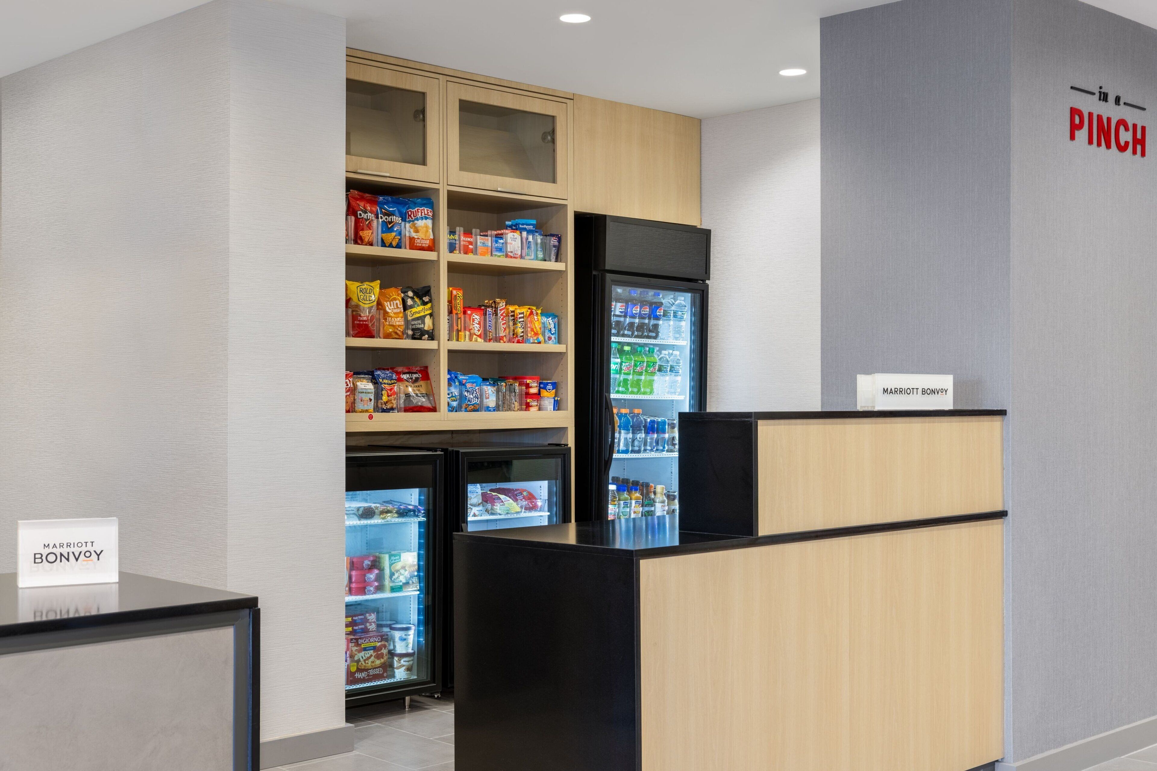 A hotel reception area with a self-service snack machine stocked with various snacks and a refrigerator.