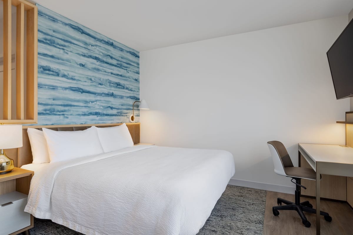 A hotel room with a large bed, a desk, a chair, and a TV.