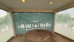 Ein Zimmer mit einem großen Fenster, einem Korbssesselsofa und einer Wand mit dem Schriftzug 'The Bellal Vita Resort'.