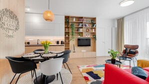 A modern living room with a red sofa, a dining area with a round table and chairs, a kitchen with a built-in TV, and a bookshelf. - On the Danube, city center, free parking (Bratislava)