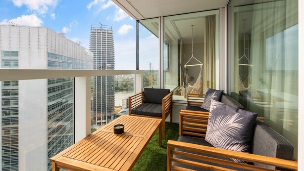 A balcony with a wooden table and chairs, a hanging light fixture, and a view of city buildings. - On the Danube, city center, free parking (Bratislava)