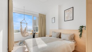 A bedroom with a bed, a hanging chair, a window with curtains, a framed picture on the wall, and a plant. - On the Danube, city center, free parking (Bratislava)
