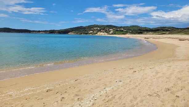Una playa con aguas azules cristalinas, orilla de arena y un paisaje montañoso al fondo.