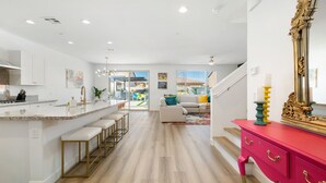 A modern kitchen with a central island, a dining area with bar stools, a living room with a sofa and colorful cushions, and a staircase leading to another level. - Eclectic Paradise w/Pool & Spa! Close to Festivals (Coachella)
