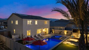A modern two-story house with a swimming pool, outdoor seating, and a well-lit patio area. - Eclectic Paradise w/Pool & Spa! Close to Festivals (Coachella)
