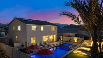 A modern two-story house with a swimming pool, outdoor seating, and a well-lit patio area.