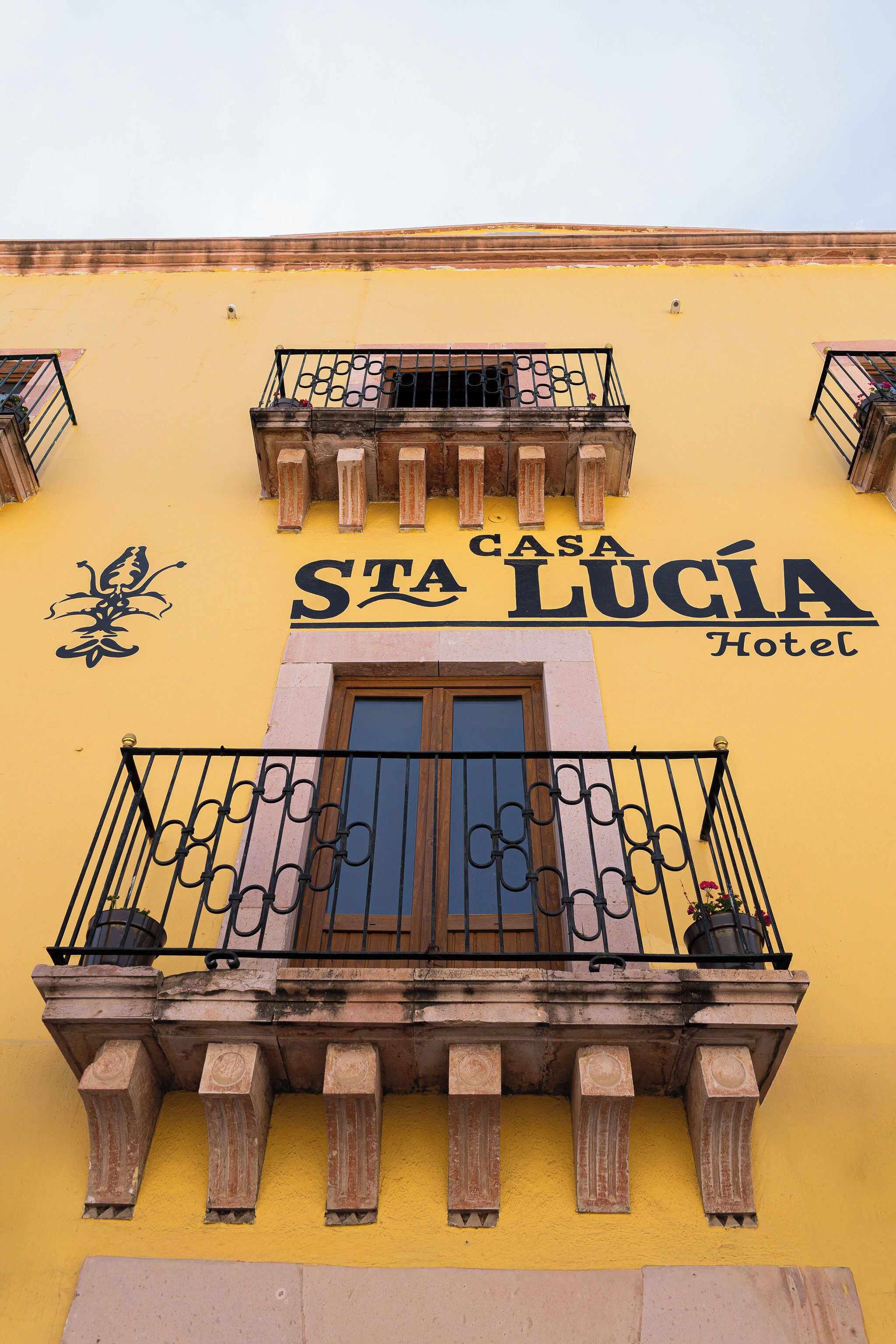 A building with a yellow facade, balconies with wrought iron railings, and a sign that reads 'Casa Lucía Hotel.'