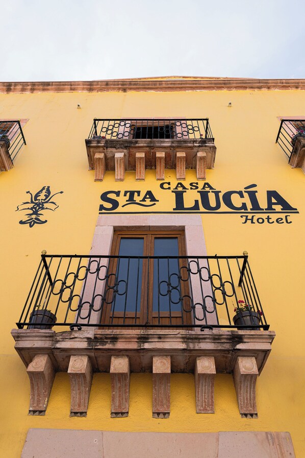 Un edificio con fachada amarilla, balcones con barandillas de hierro forjado y un letrero que dice 'Casa Lucía Hotel'.