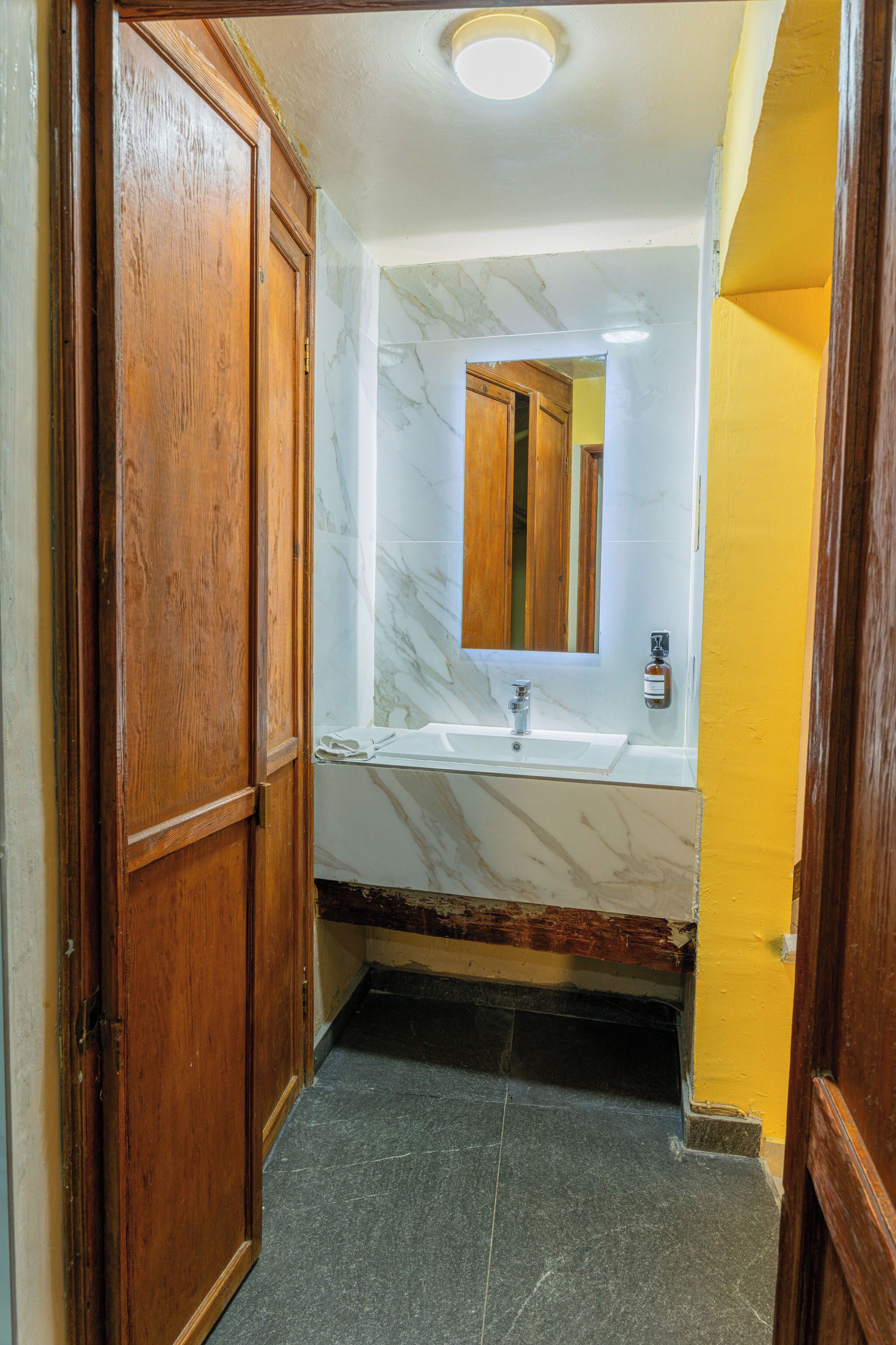 A bathroom with a wooden door, a marble sink, and a mirror.