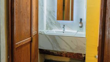 Un baño con puerta de madera, lavamanos de mármol y espejo.