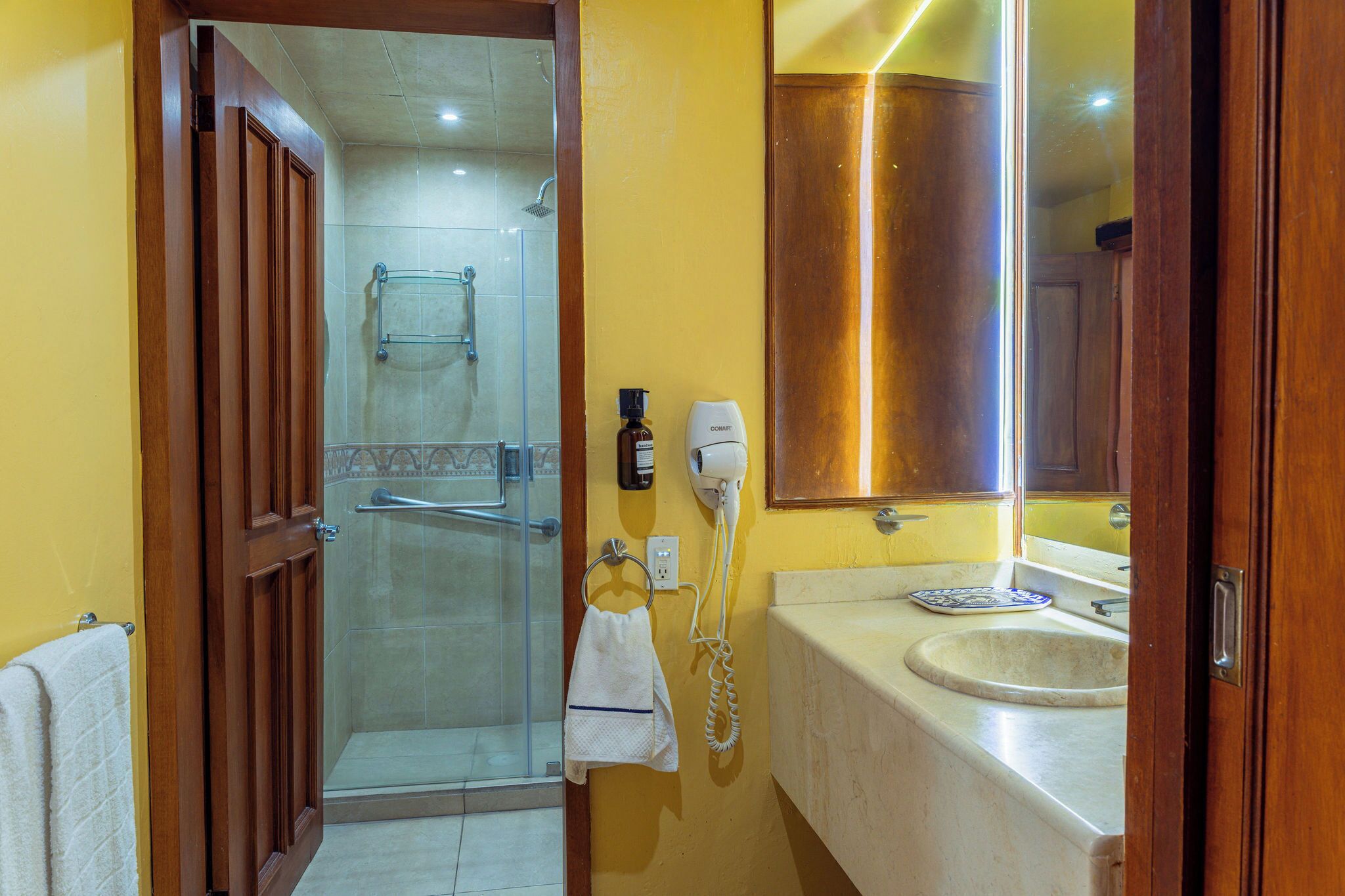 Een badkamer met een glazen douche, een wastafel, een handdoekrek en een haardroger.