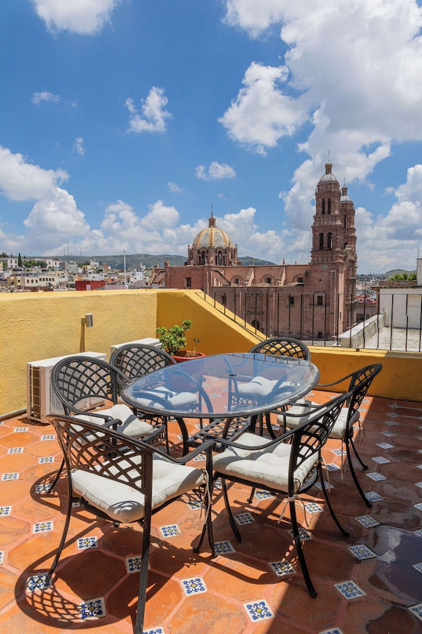 A terrace with a round table and chairs, a potted plant, and a view of a historic building with a dome and bell tower. - Hotel Casa Santa Lucia (Zacatecas)