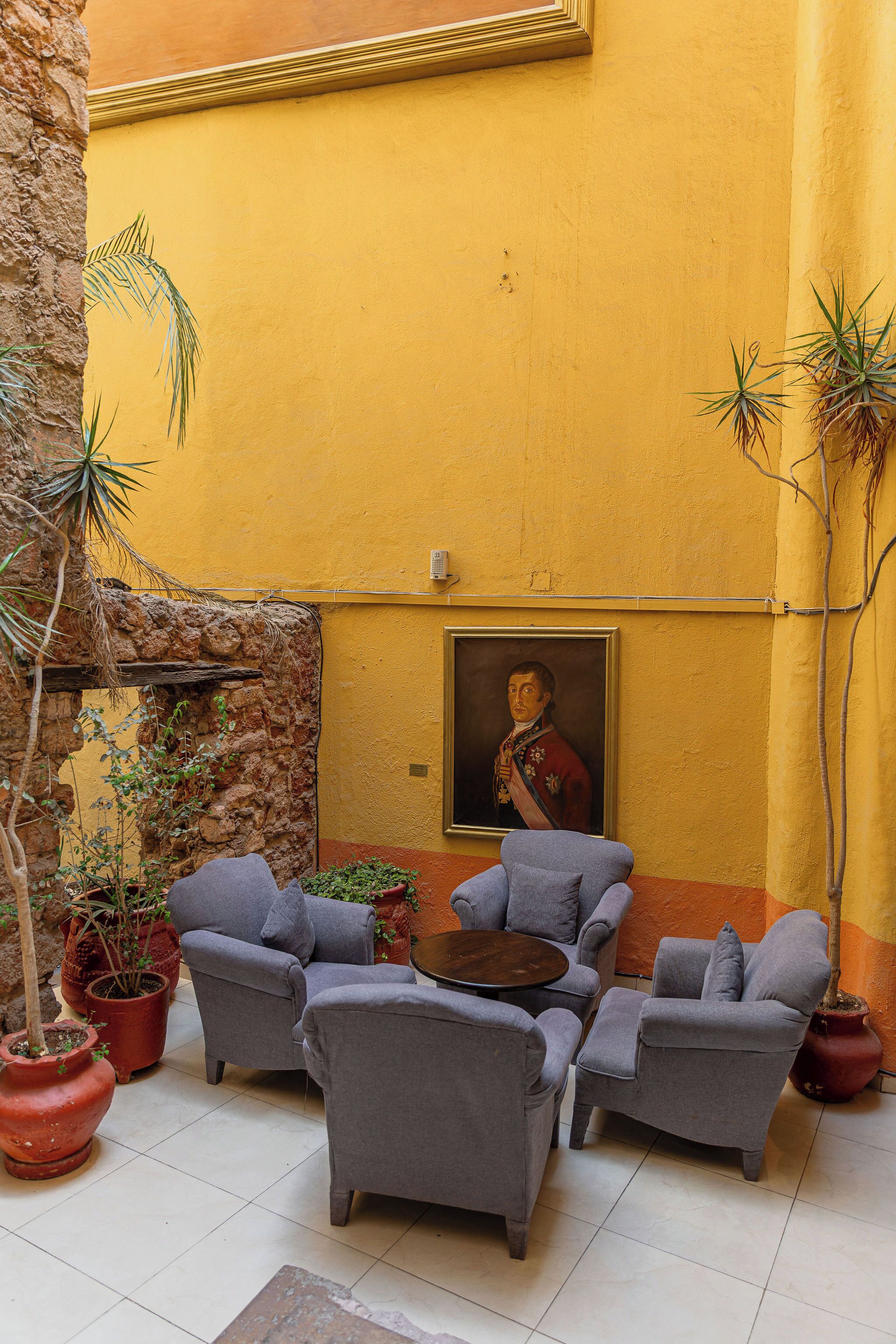 An outdoor seating area with grey sofas and a small round table, surrounded by potted plants and a stone wall.