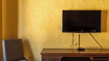 A room with a wooden desk, a chair, a flat-screen TV mounted on the wall, and an air conditioning unit above the desk.