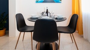 Een eethoek met een ronde tafel, zwarte stoelen en een schilderij van een meer en bergen aan de muur.
