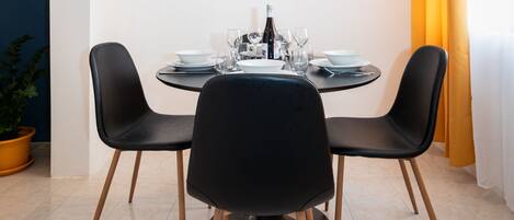 A dining area with a round table, black chairs, and a painting of a lake and mountains on the wall.