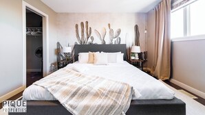 A bedroom with a large bed, a wardrobe, and a cactus wall decoration. - 4BDRM Chic Home - King Bed - BBQ - Garage - WiFi (Edmonton)