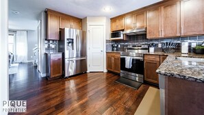 A modern kitchen with wooden cabinets, stainless steel appliances, and a granite countertop. - 4BDRM Chic Home - King Bed - BBQ - Garage - WiFi (Edmonton)