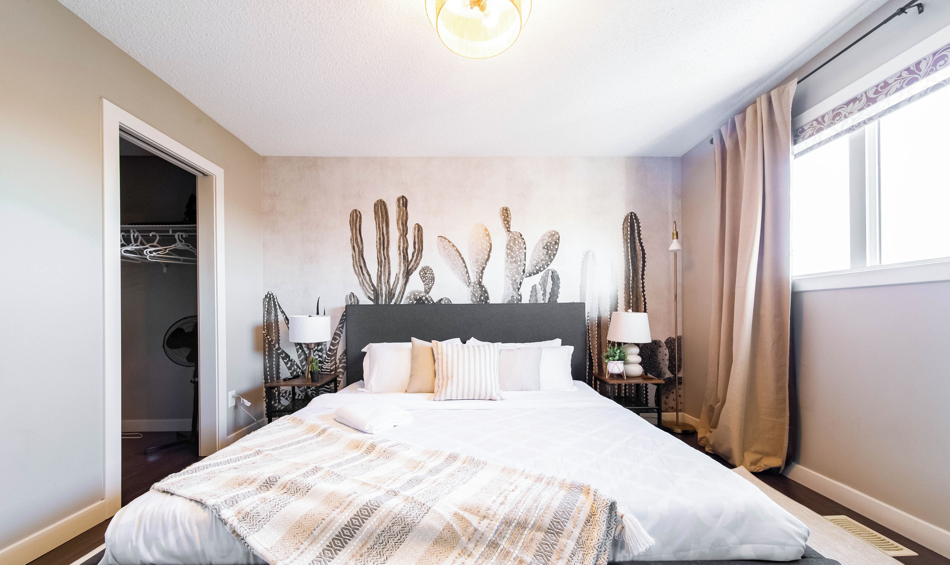 A bedroom with a large bed, a wardrobe, and a cactus wall decoration.