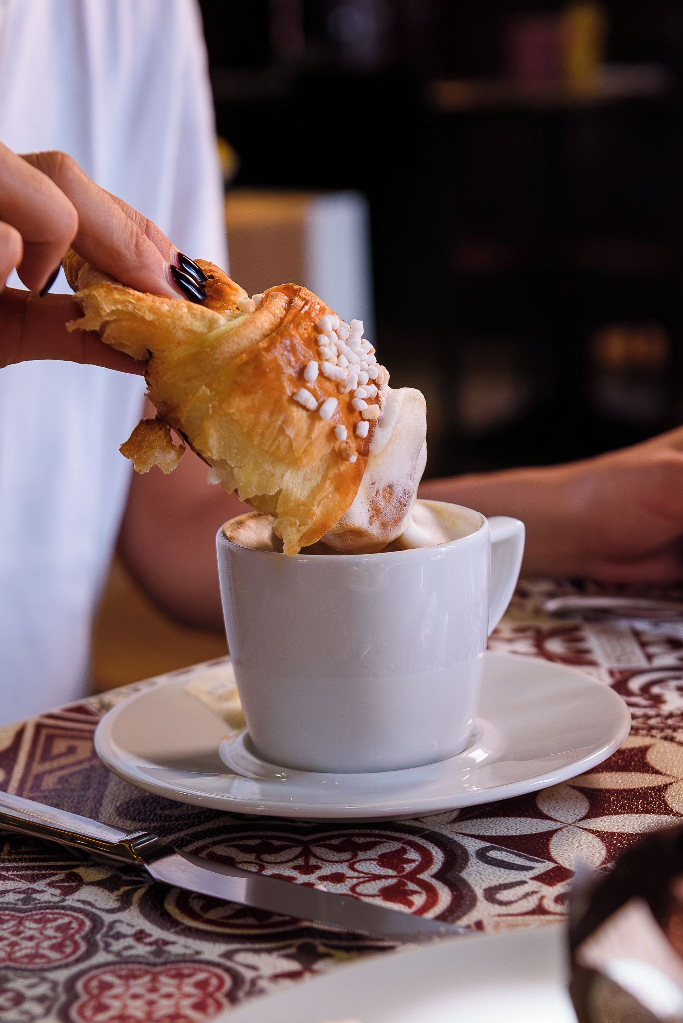 Una mano sosteniendo un pastel sobre una taza de café.