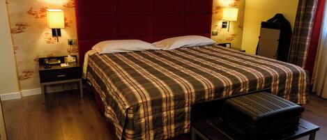 A hotel room with a bed, bedside tables, a lamp, a suitcase, and a mirror.