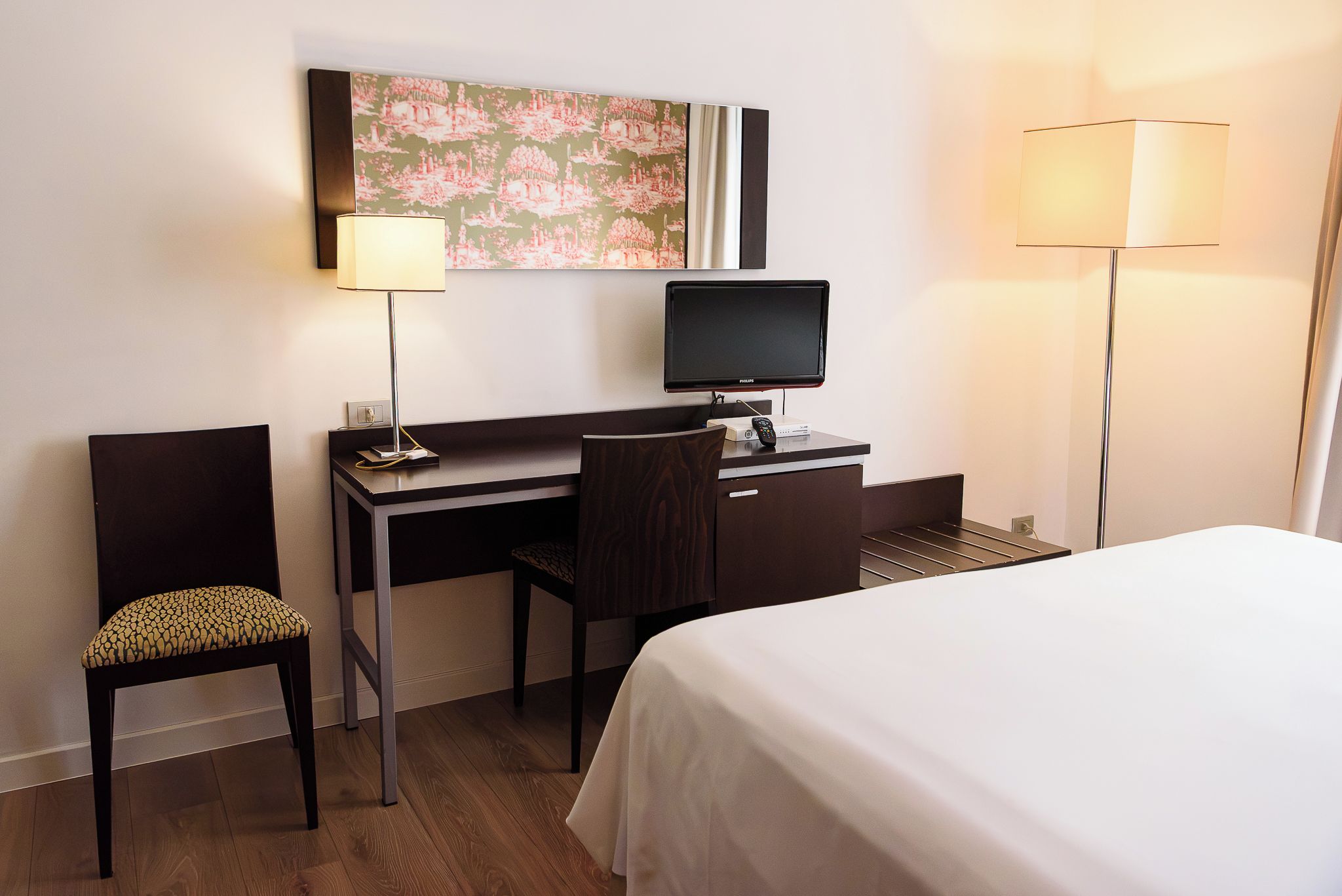 Ein Hotelzimmer mit einem Bett, einem Schreibtisch, einem Sessel, einem Fernseher und zwei Lampen.