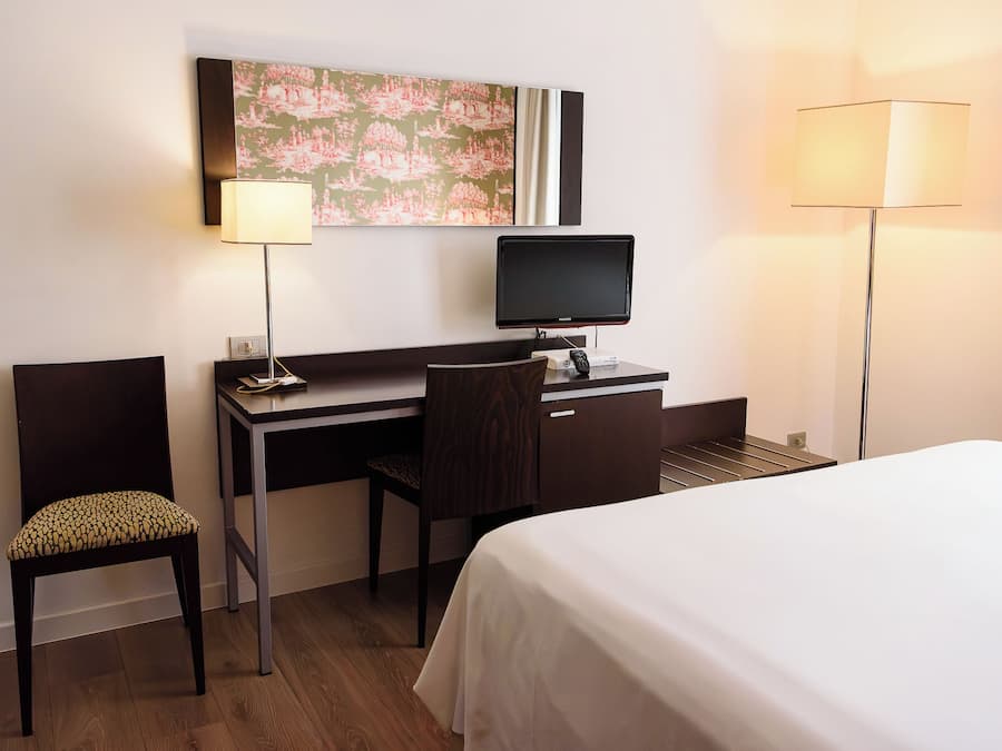 Una habitación de hotel con una cama, un escritorio, una silla, un televisor y dos lámparas.