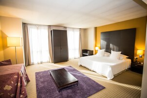 Quarto de hotel com cama, escrivaninha, cadeira, mesa de cabeceira, abajur e guarda-roupa.