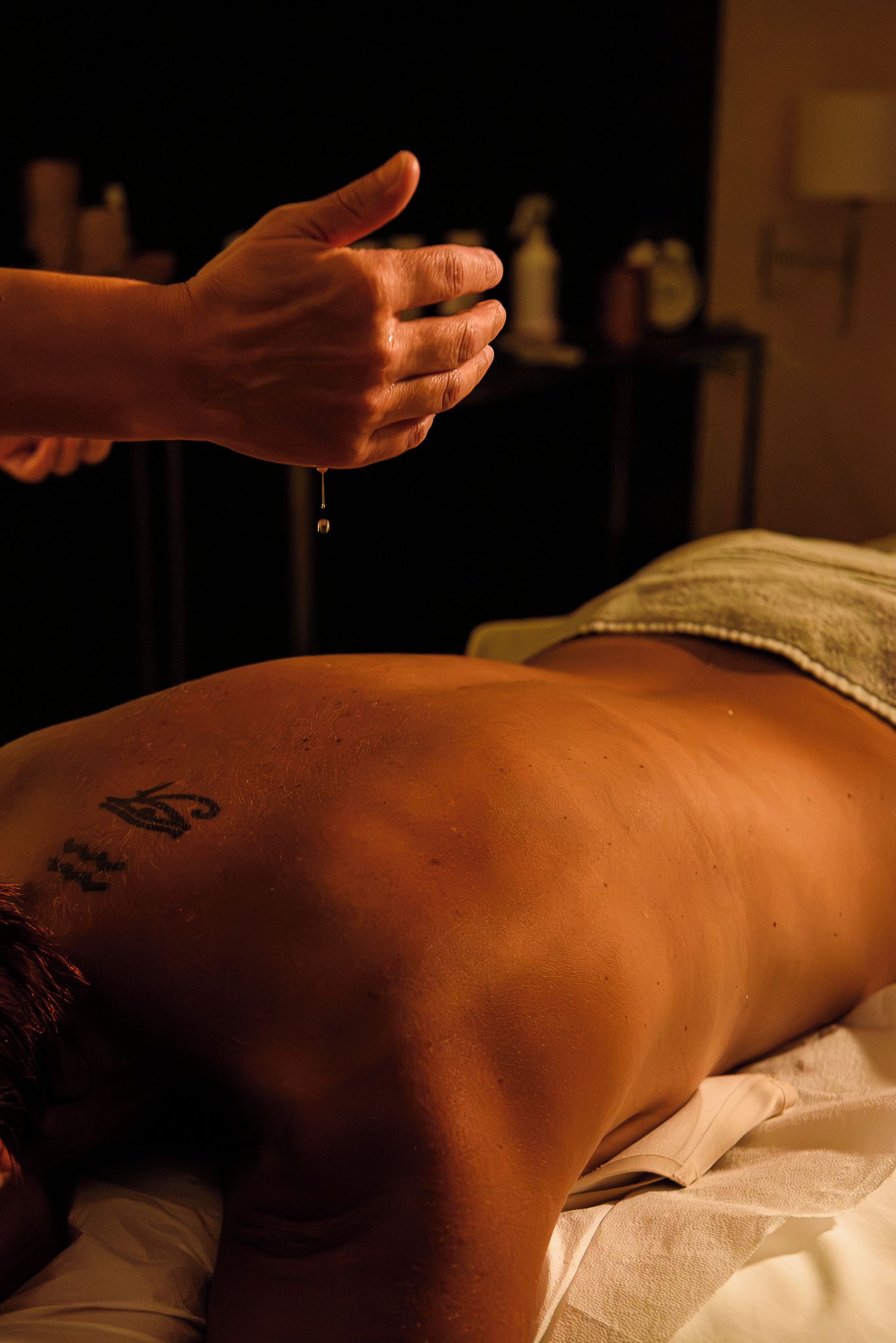 A person lying on a bed with a towel, receiving a treatment with a dropper.