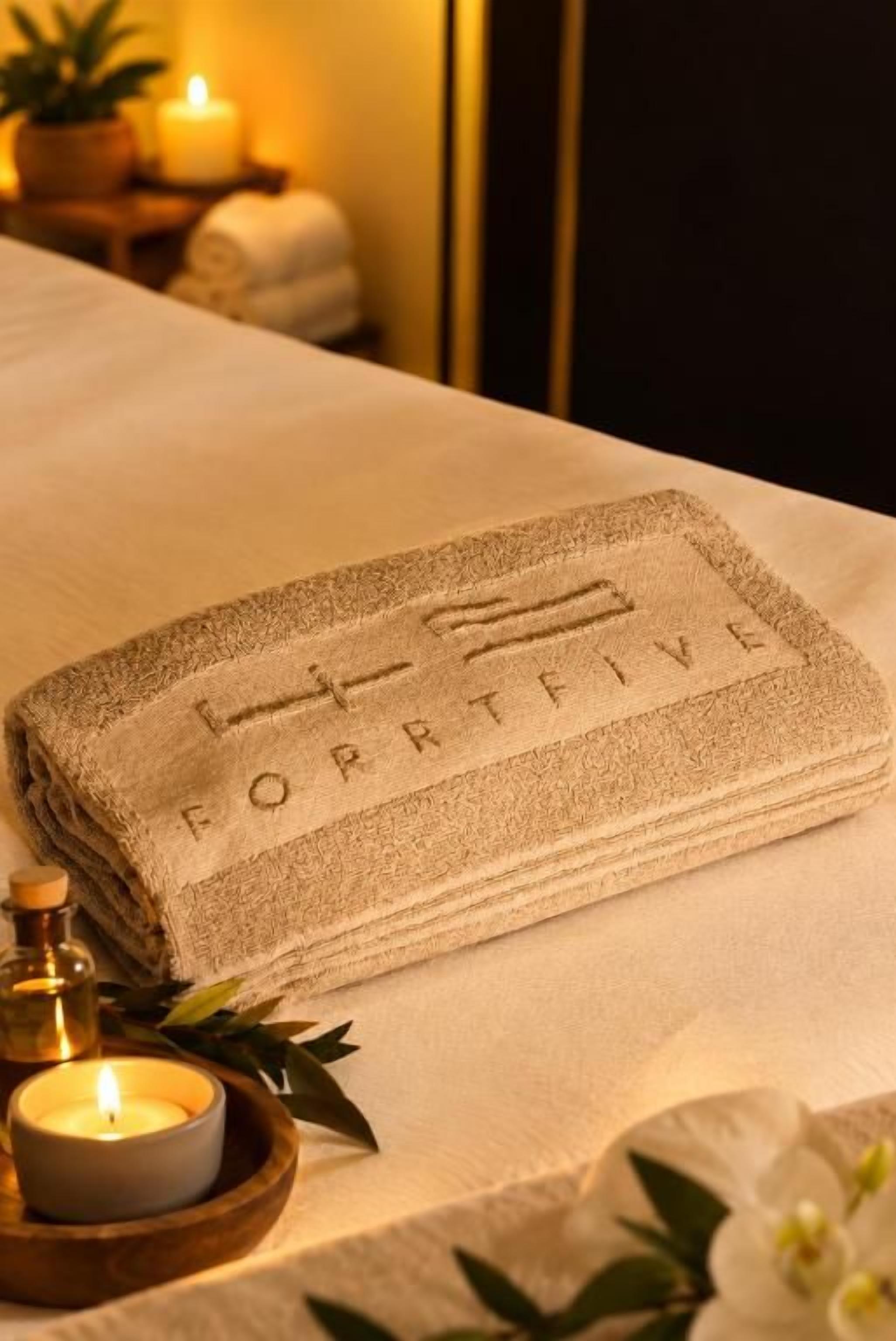 A neatly folded towel with the inscription 'FORPTFIVE' on a bed.